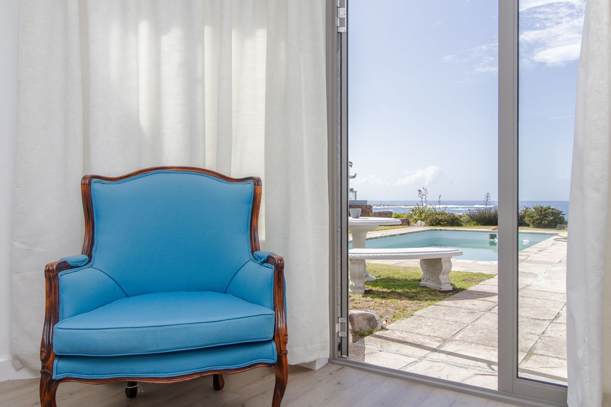 Een blauwe fauteuil bij een schuifpui met uitzicht op een zwembad en een terras.