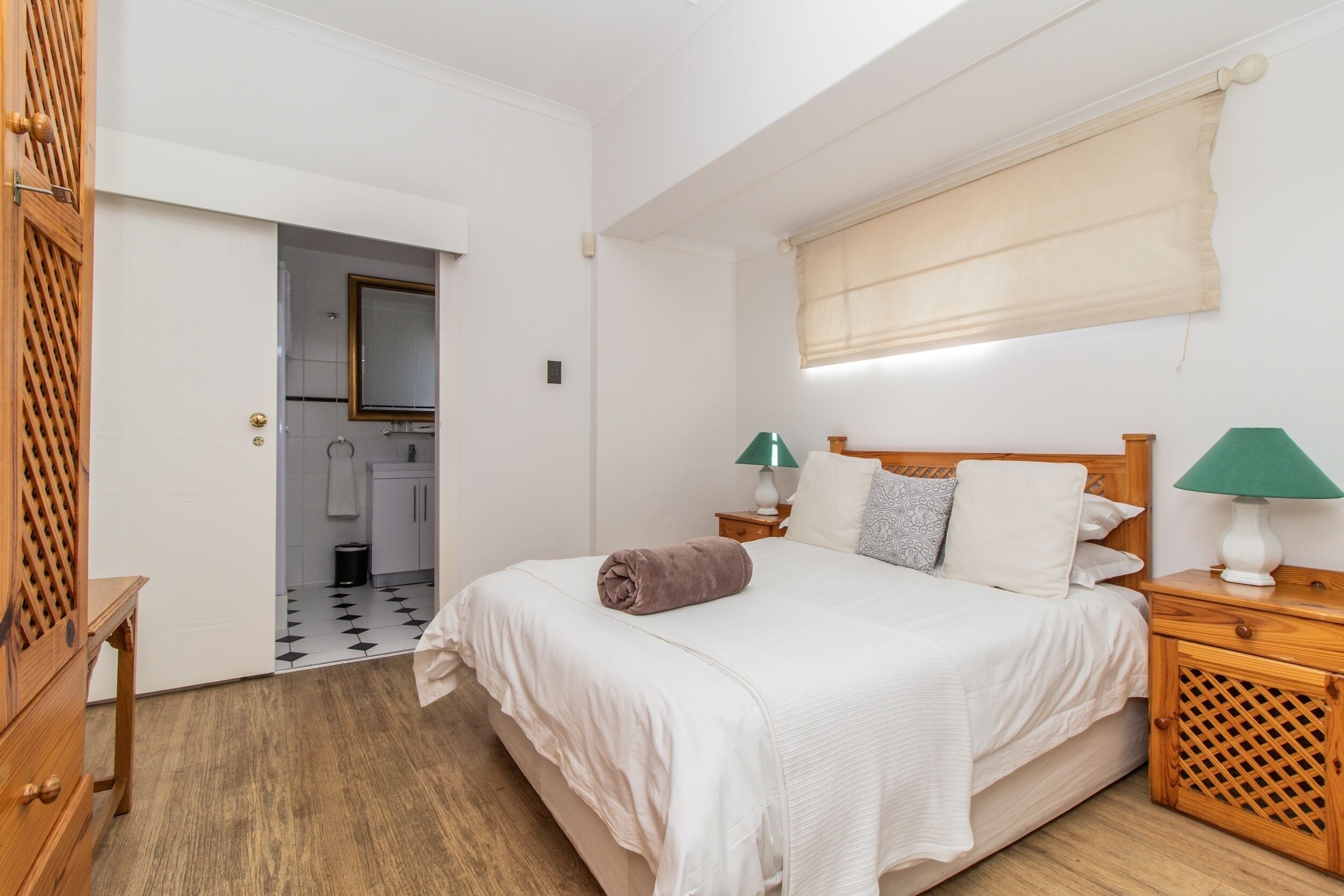 Ein Schlafzimmer mit einem Bett, Nachttischen aus Holz, einem Spiegel und einem Fenster mit Jalousie.