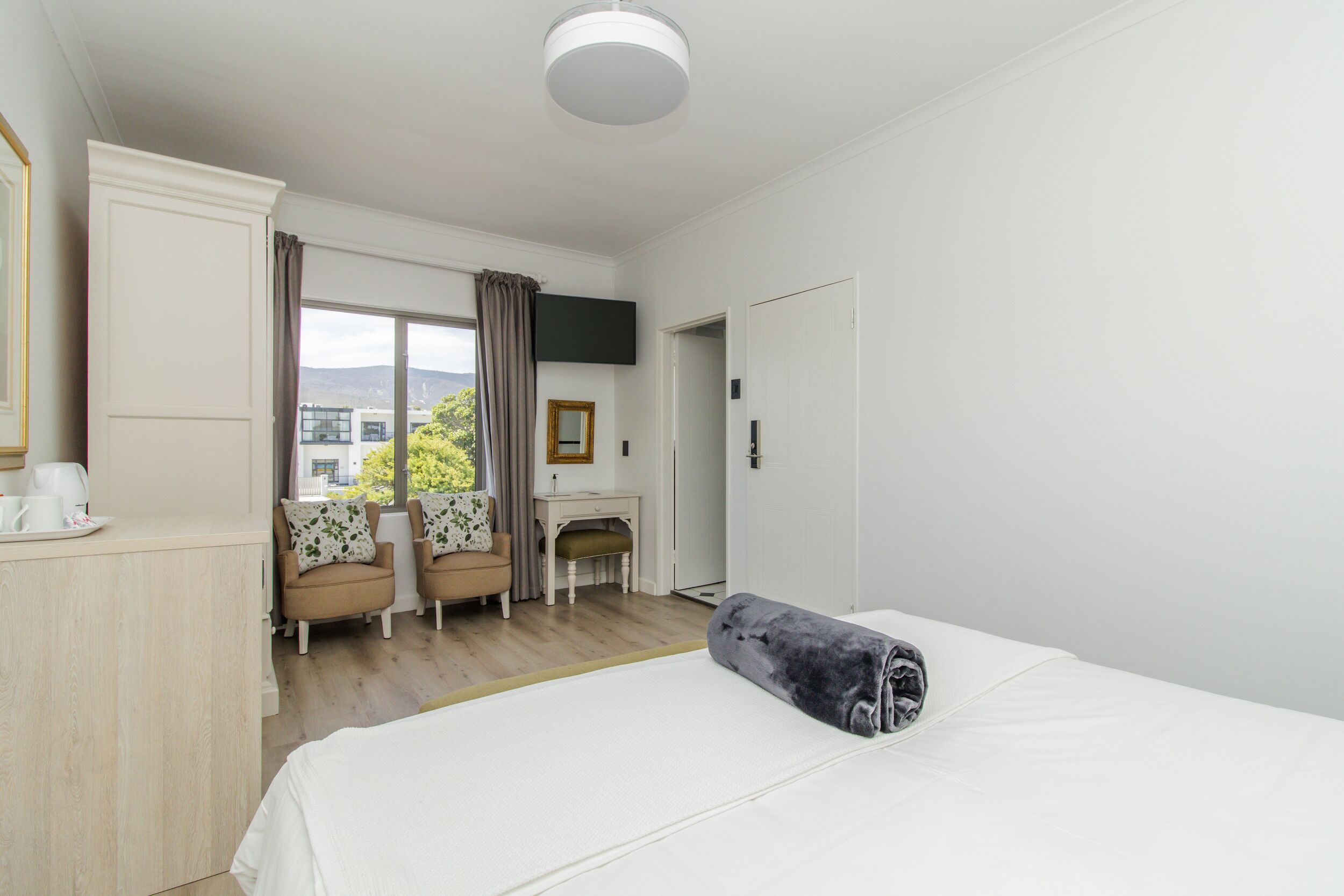 A hotel room with a bed, a desk, two chairs, a TV, and a view of the outdoors.