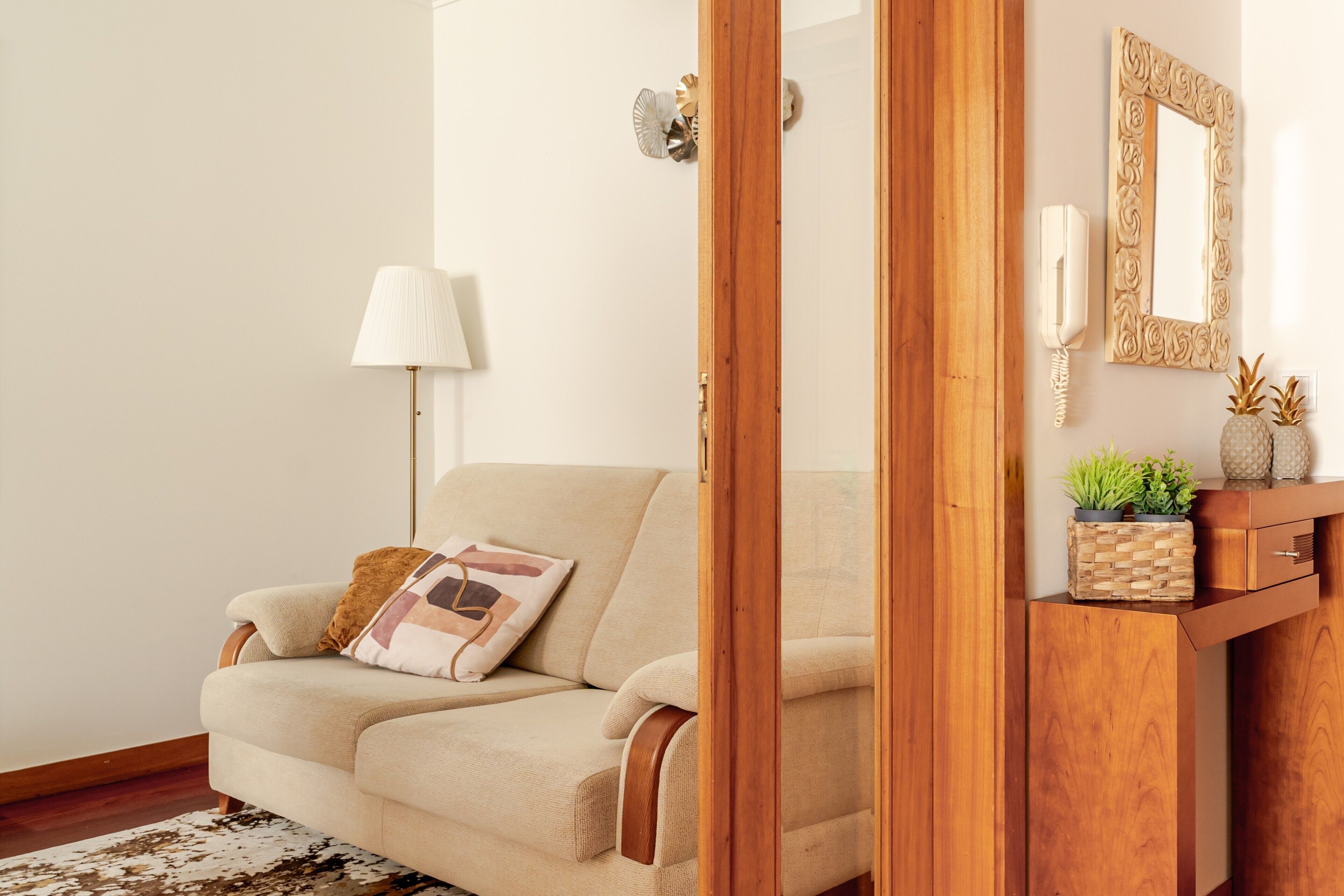 Ein Wohnzimmer mit einem beigefarbenen Sofa, einem Holzschrank, einer Lampe und einem dekorativen Spiegel.