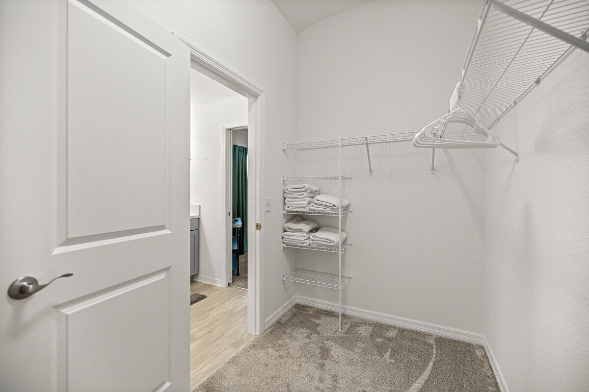 Un angolo di stanza con una porta bianca, un armadio bianco con ripiani e un tappeto grigio.