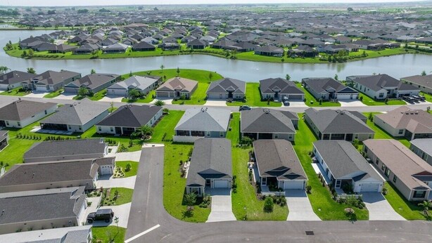 Un barrio residencial con casas alineadas en hileras a lo largo de una carretera curva, y un lago al fondo.