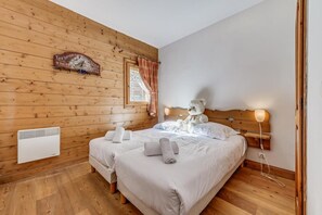 A cozy bedroom with a wooden ceiling, a bed with white linens, a teddy bear on the bed, and a wall-mounted heater. - 3rd floor, fitness, swimming pool, sauna, hammam, terrace, parking, tv, 57m², Champagny-en-Vanoise (Champagny-en-Vanoise)