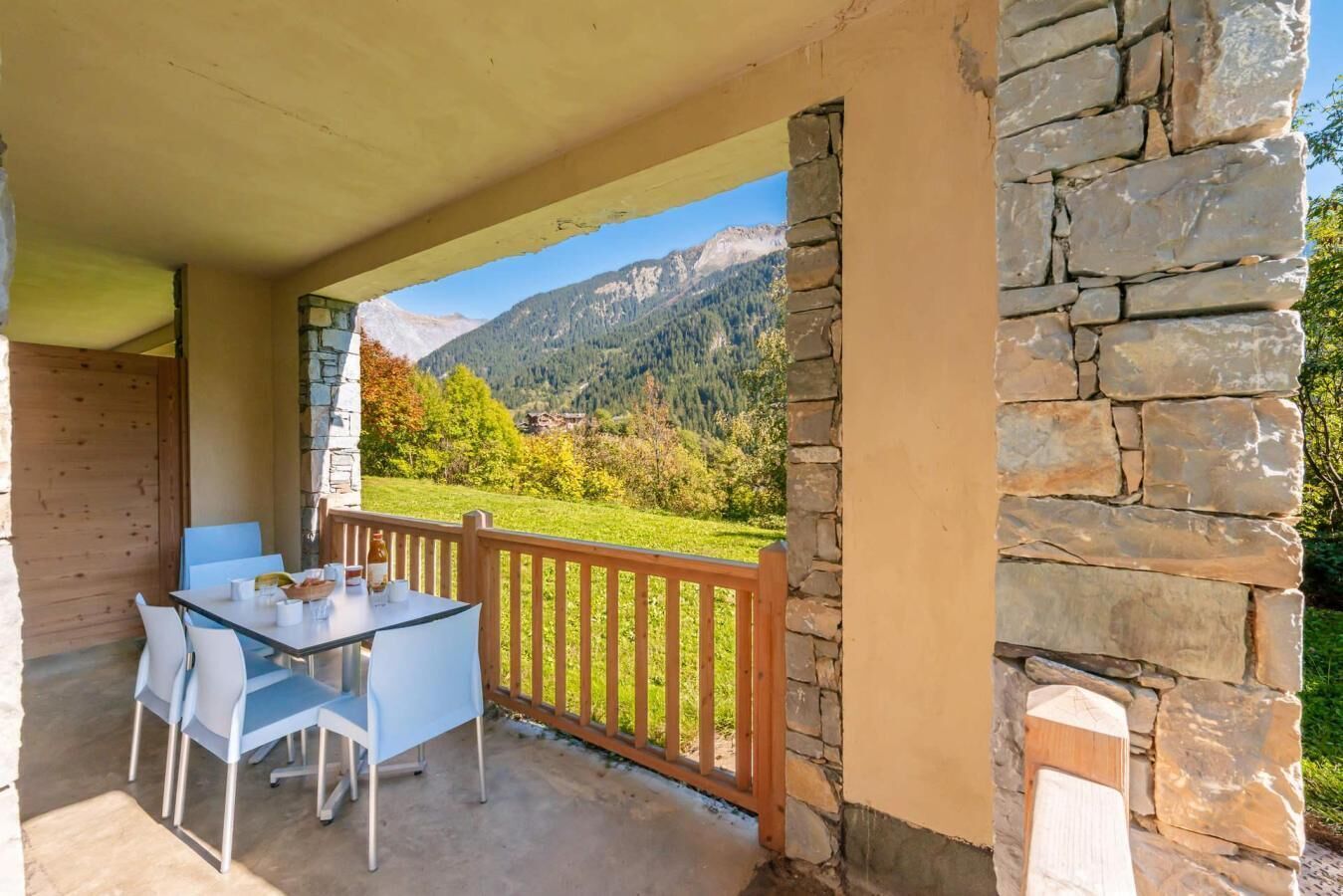 A covered outdoor seating area with a table and chairs, stone walls, and a view of a mountainous landscape.