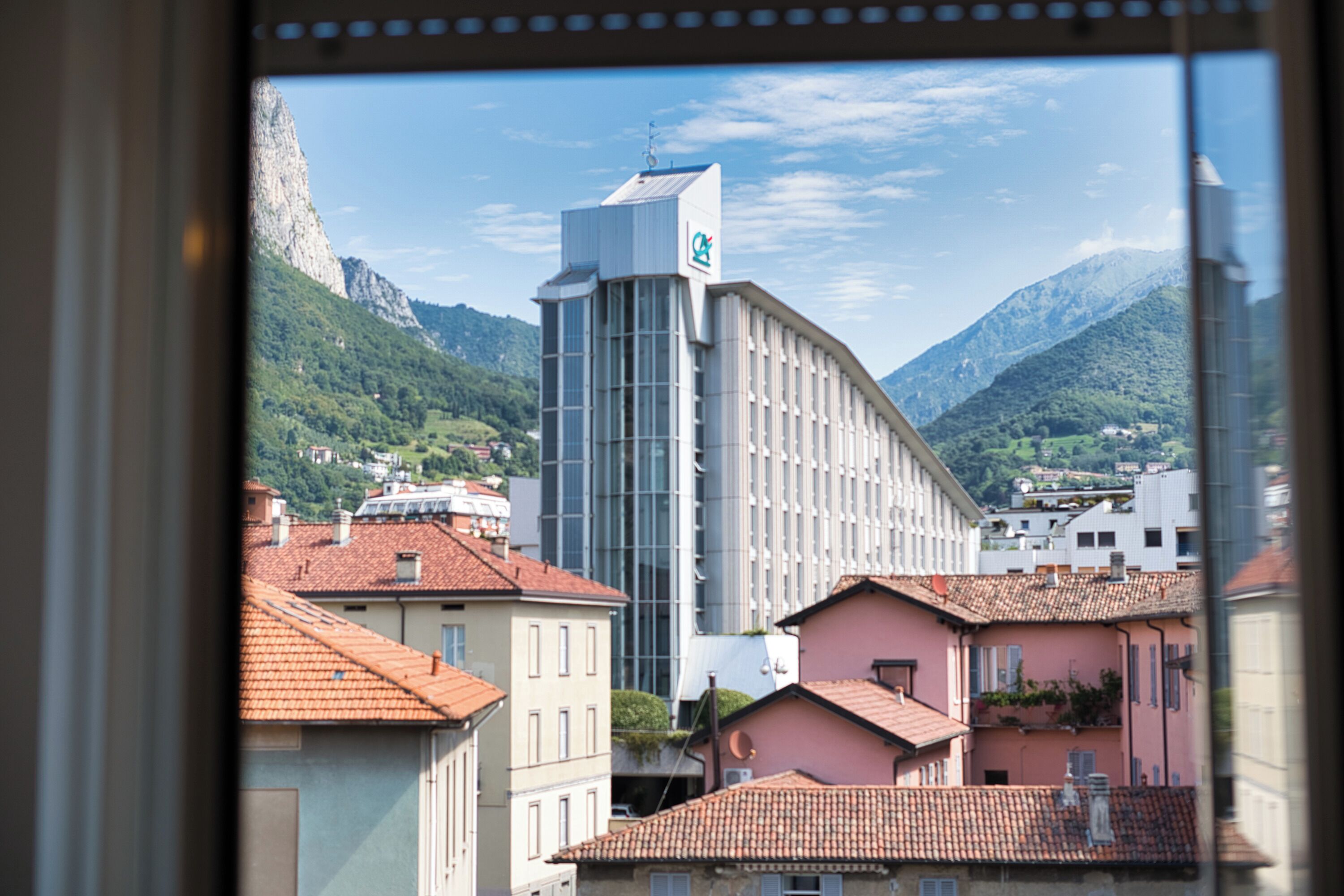 Une vue d’un bâtiment à l’architecture moderne, entouré d’édifices traditionnels et avec des montagnes en arrière-plan.
