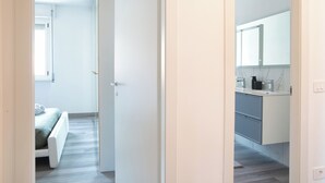 A modern hotel room with a bed, a bathroom with a large mirror, and a view of the hallway. - Royal Suite - Lake Como (Lecco)