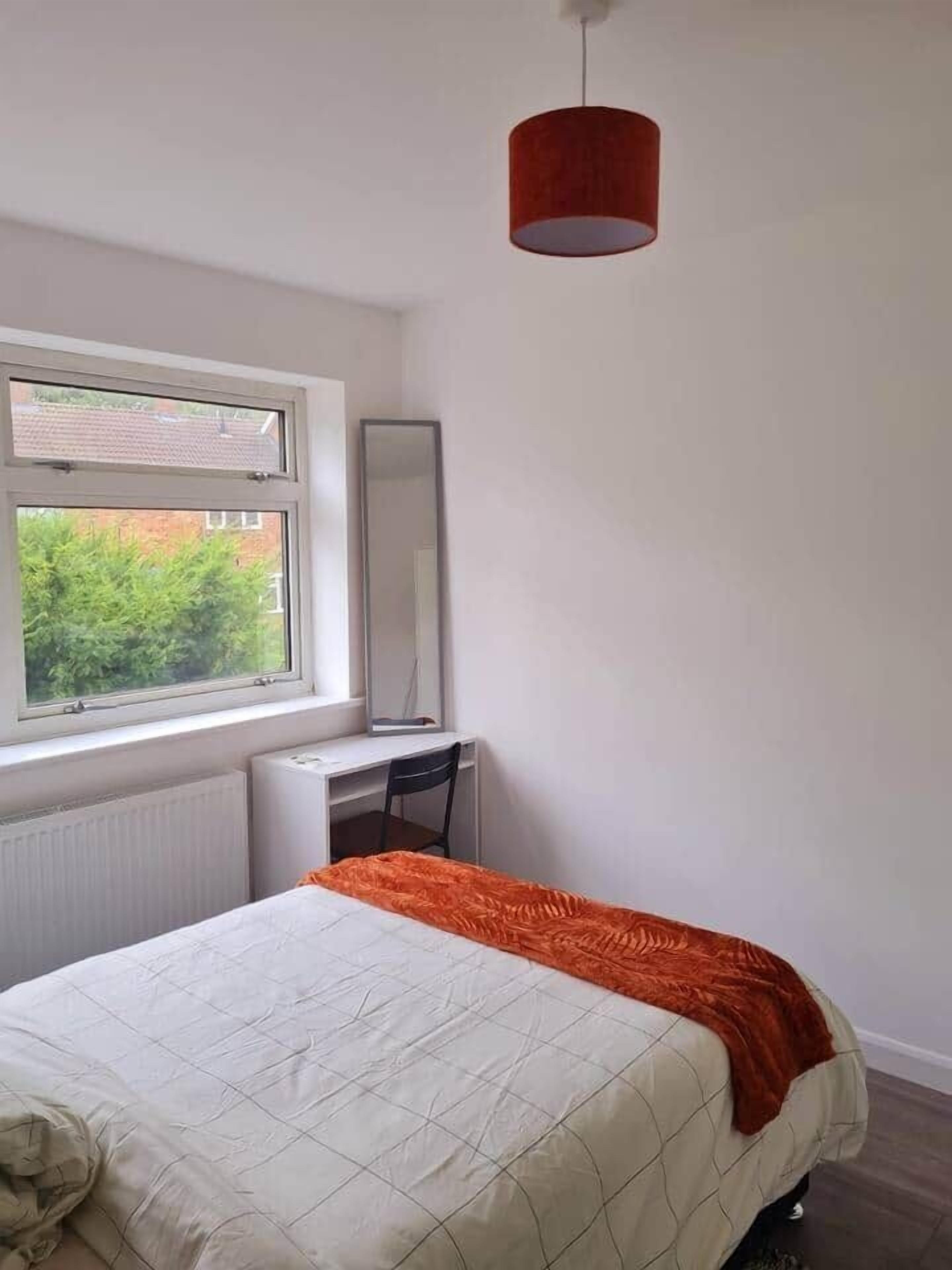 A bedroom with a bed, a desk, a chair, a window, and a red hanging light fixture.
