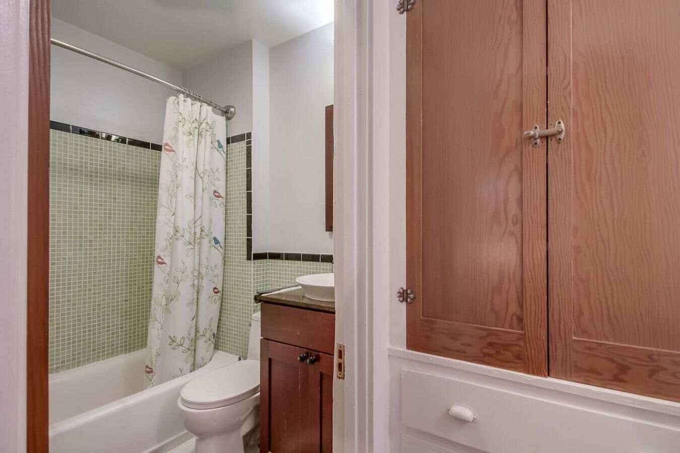 A bathroom with a bathtub, toilet, and a wooden cabinet.