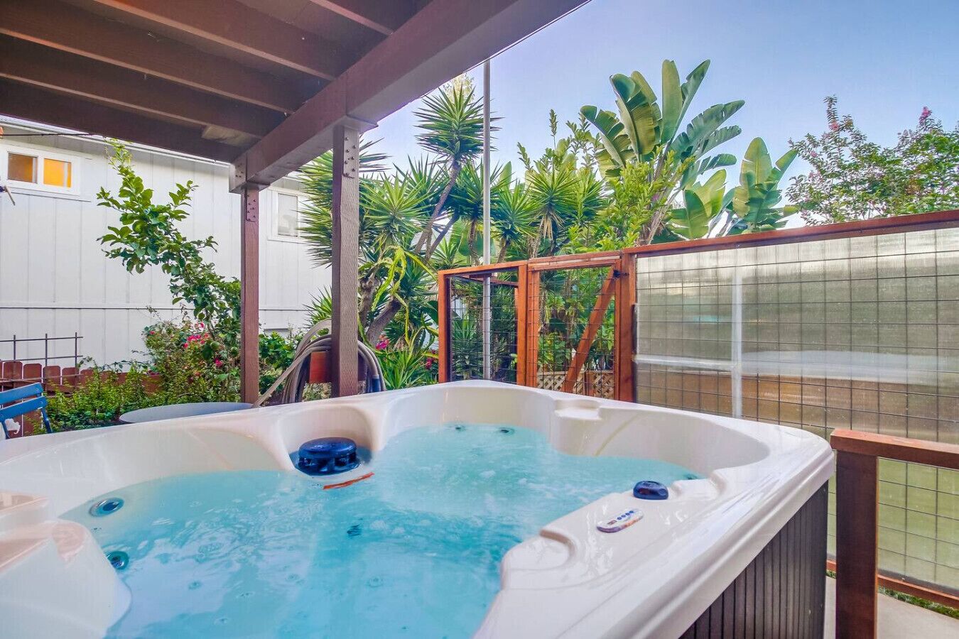 A hot tub in a covered outdoor area with a wooden deck and lush tropical plants.