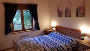 Ein Schlafzimmer mit Bett, Nachttisch, einem Fenster mit Vorhängen und zwei an der Wand befestigten Bildern.