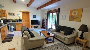 Ein Wohnzimmer mit zwei Sofas, einem Couchtisch, einem Fernseher und einer Küchenzeile mit Holzschränken und einem Esstisch.