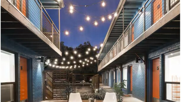 An outdoor patio area with two white plastic chairs, a small round table, and string lights overhead. - Vintage Chalet Studio 6 Creative Walkable Montrose H-Town Favorite!! (Houston)
