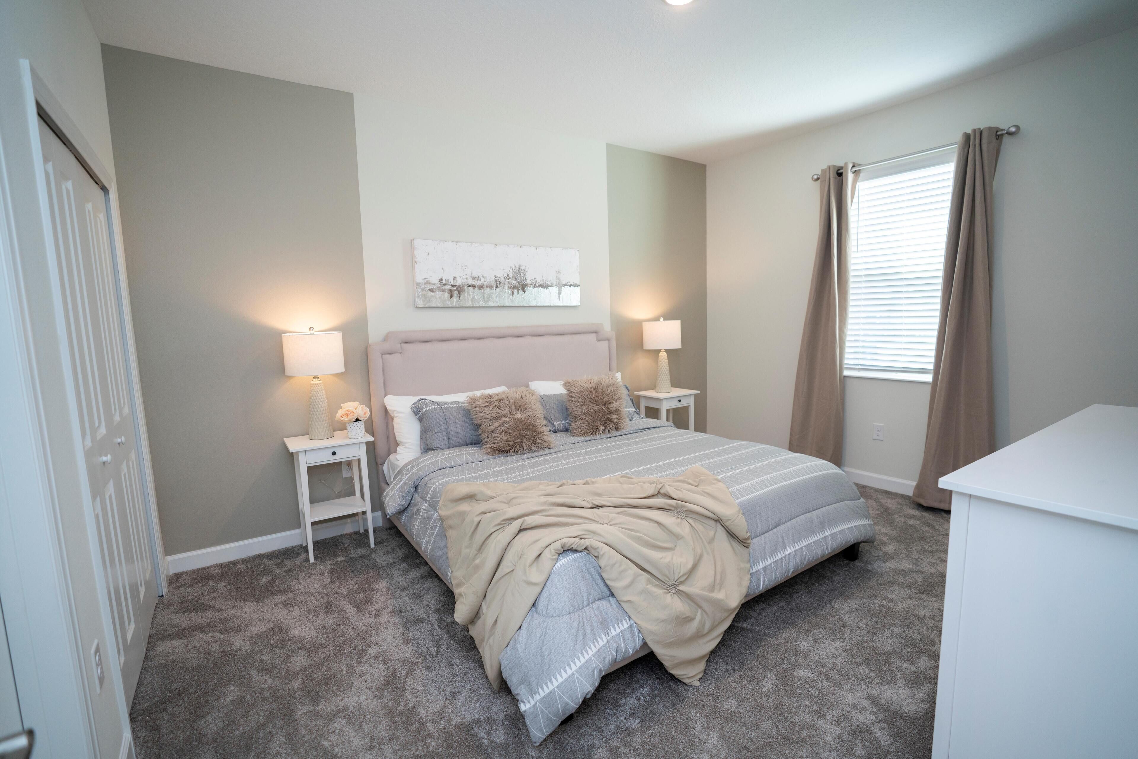 A bedroom with a bed, nightstands, a lamp, a window with curtains, and a wall-mounted artwork.
