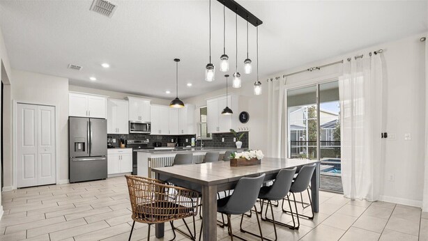 A modern kitchen with white cabinets, a stainless steel refrigerator, and a dining area with a wooden table and chairs. - 681-Sticks (Kissimmee)