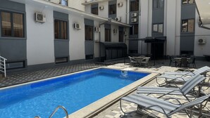 A swimming pool with lounge chairs, a barbecue area, and a building with multiple windows and air conditioning units. - Grand Zamin Hotel (Tashkent)