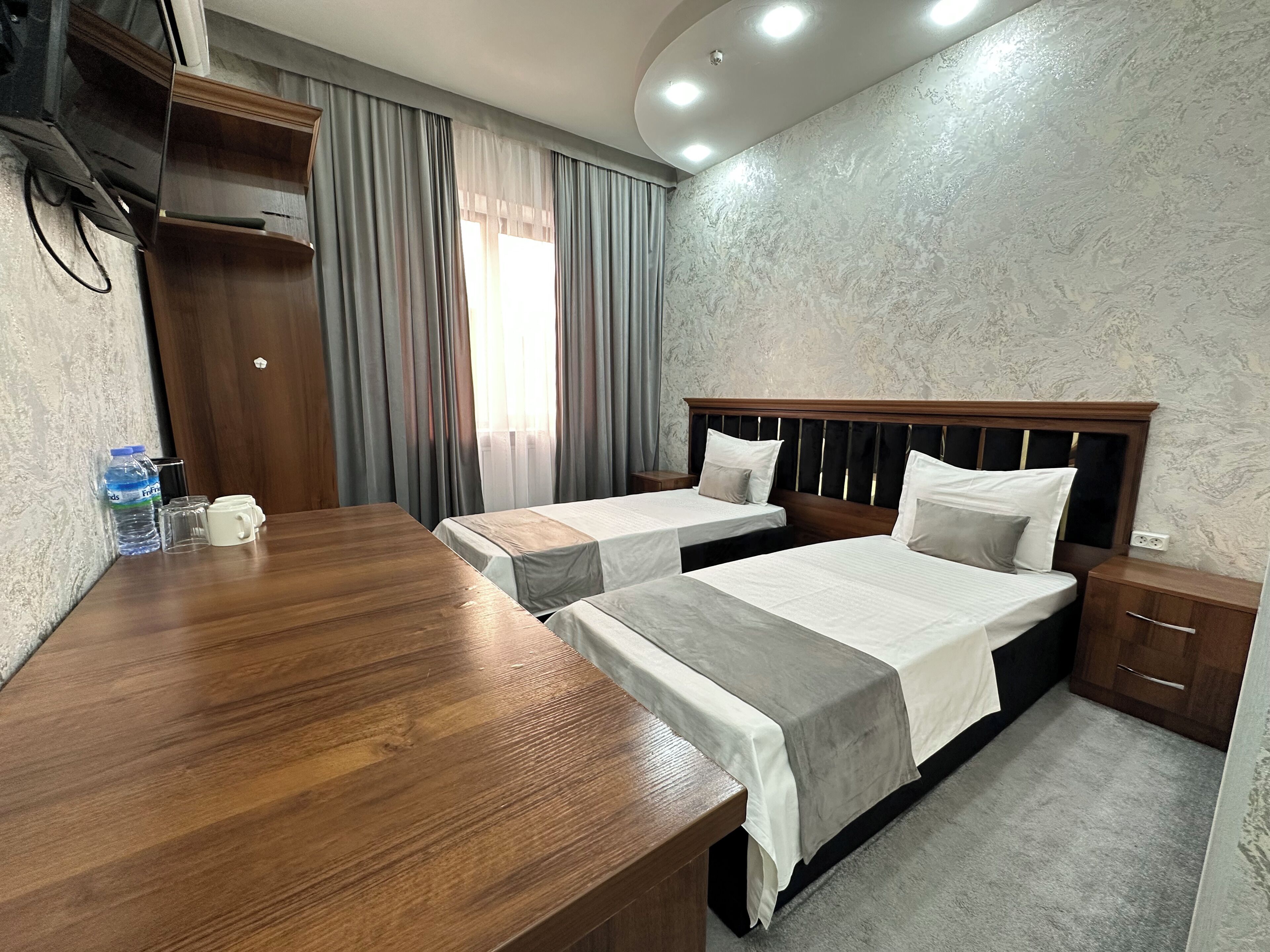 A hotel room with two beds, a wooden desk, a water bottle, and a nightstand.