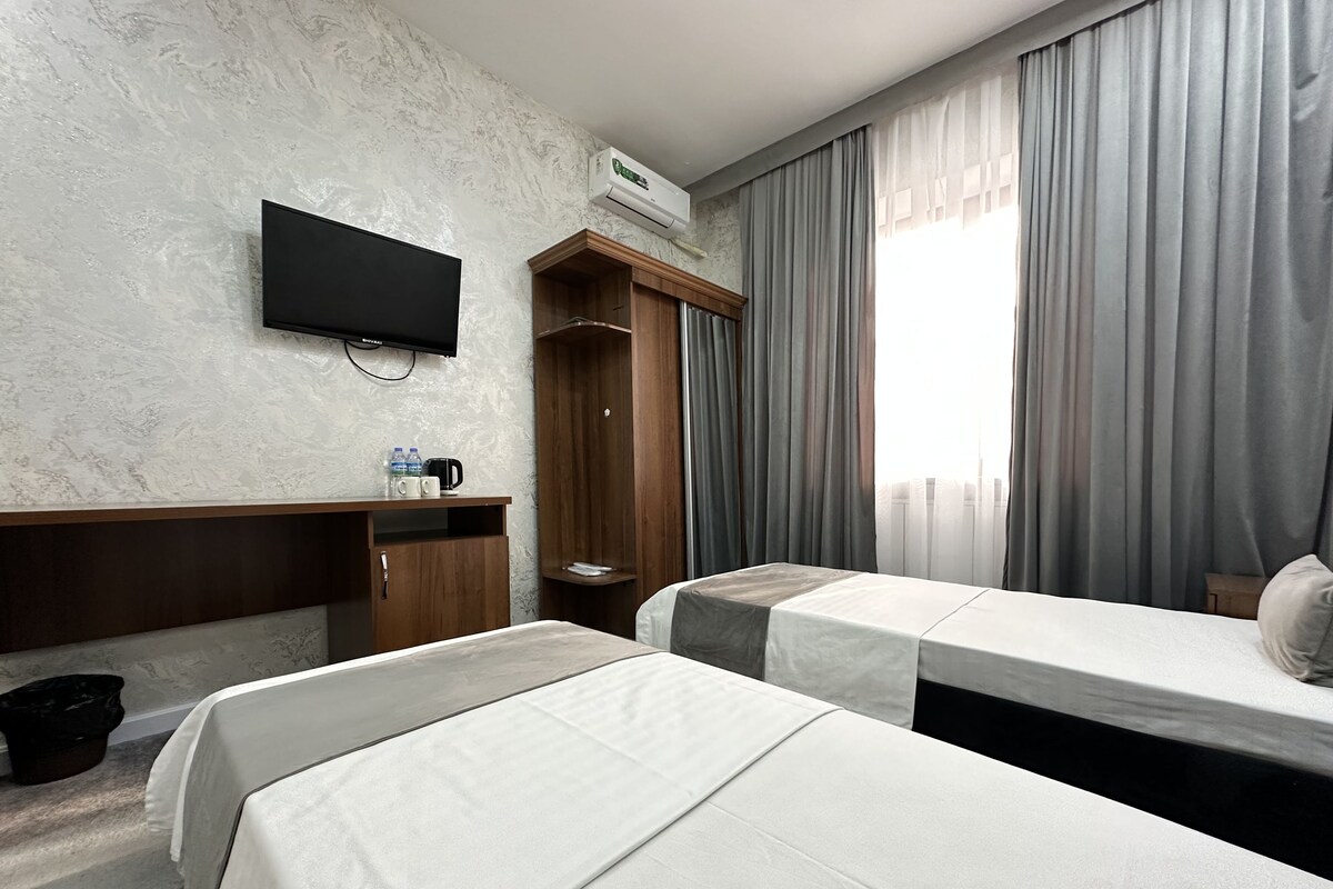 Habitación de hotel con dos camas, un televisor, un armario y una ventana con cortinas.