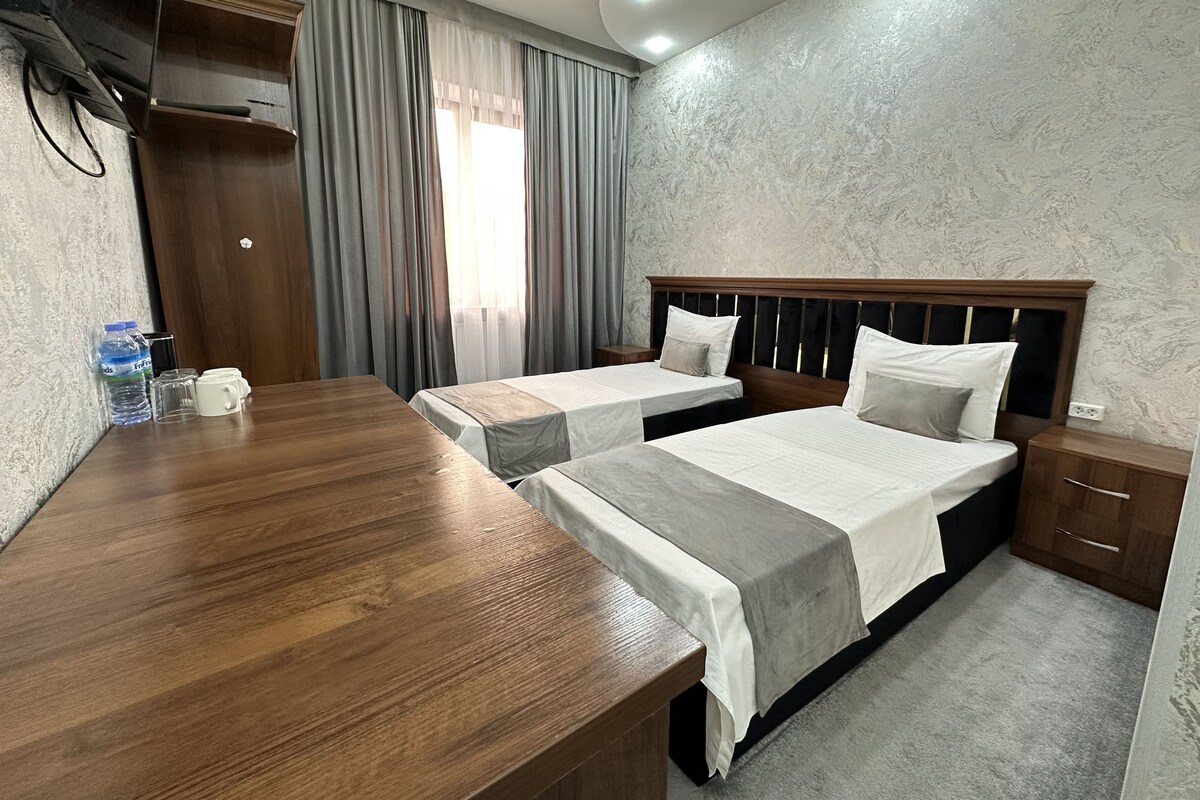 A hotel room with two beds, a wooden desk, a water bottle, and a nightstand.