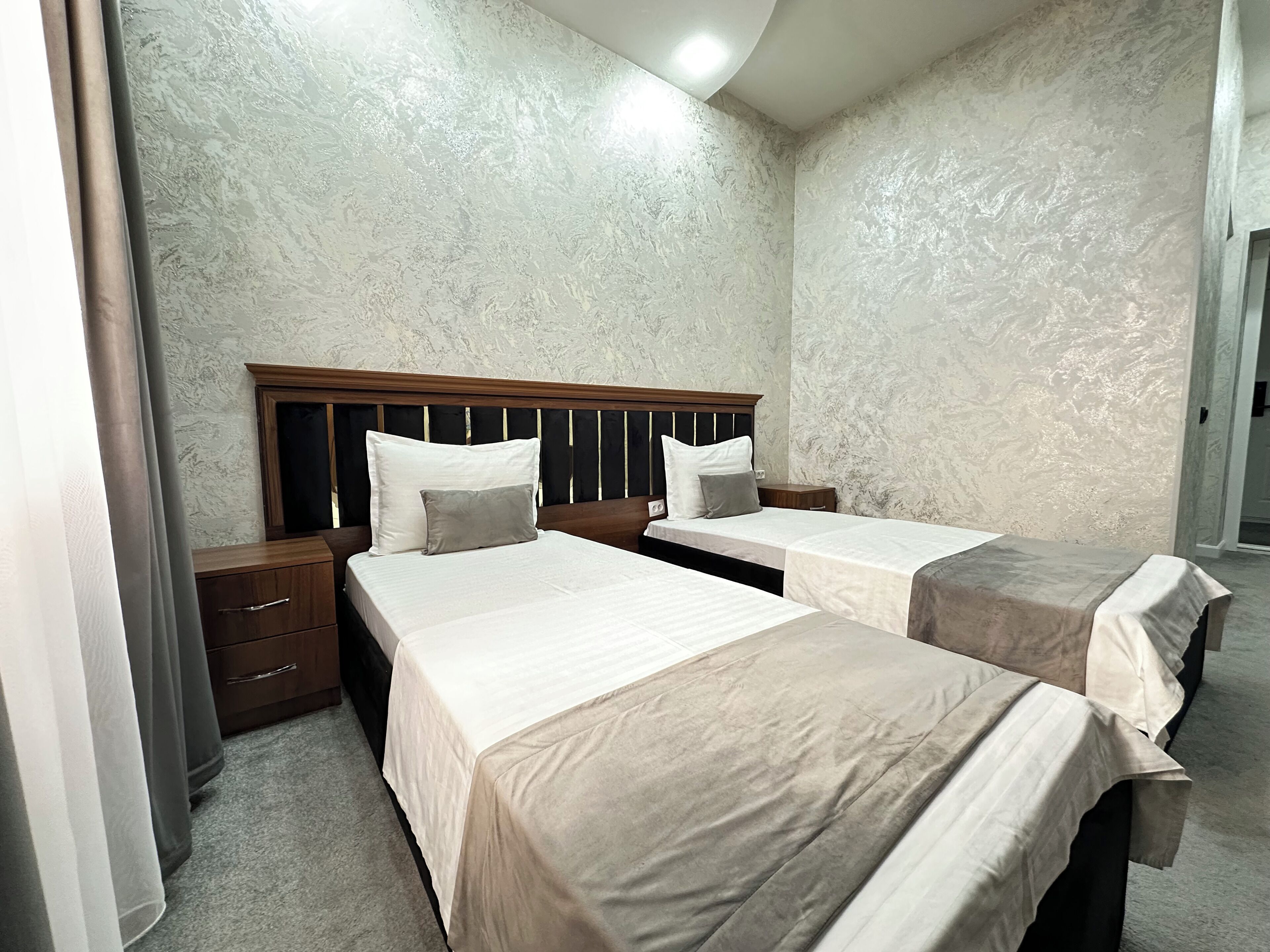 A hotel room with two beds, a wooden headboard, and a marble-patterned wall.