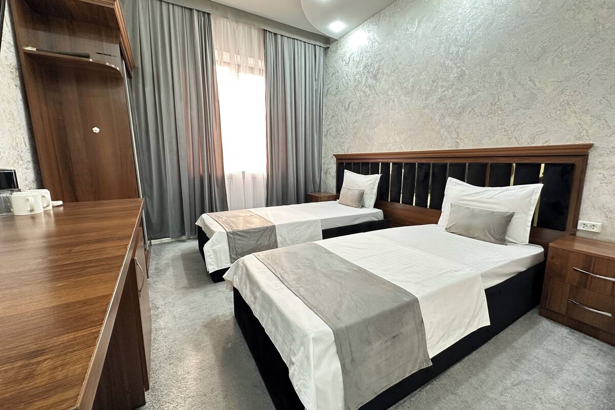 A hotel room with two beds, a wooden desk, and a wardrobe.