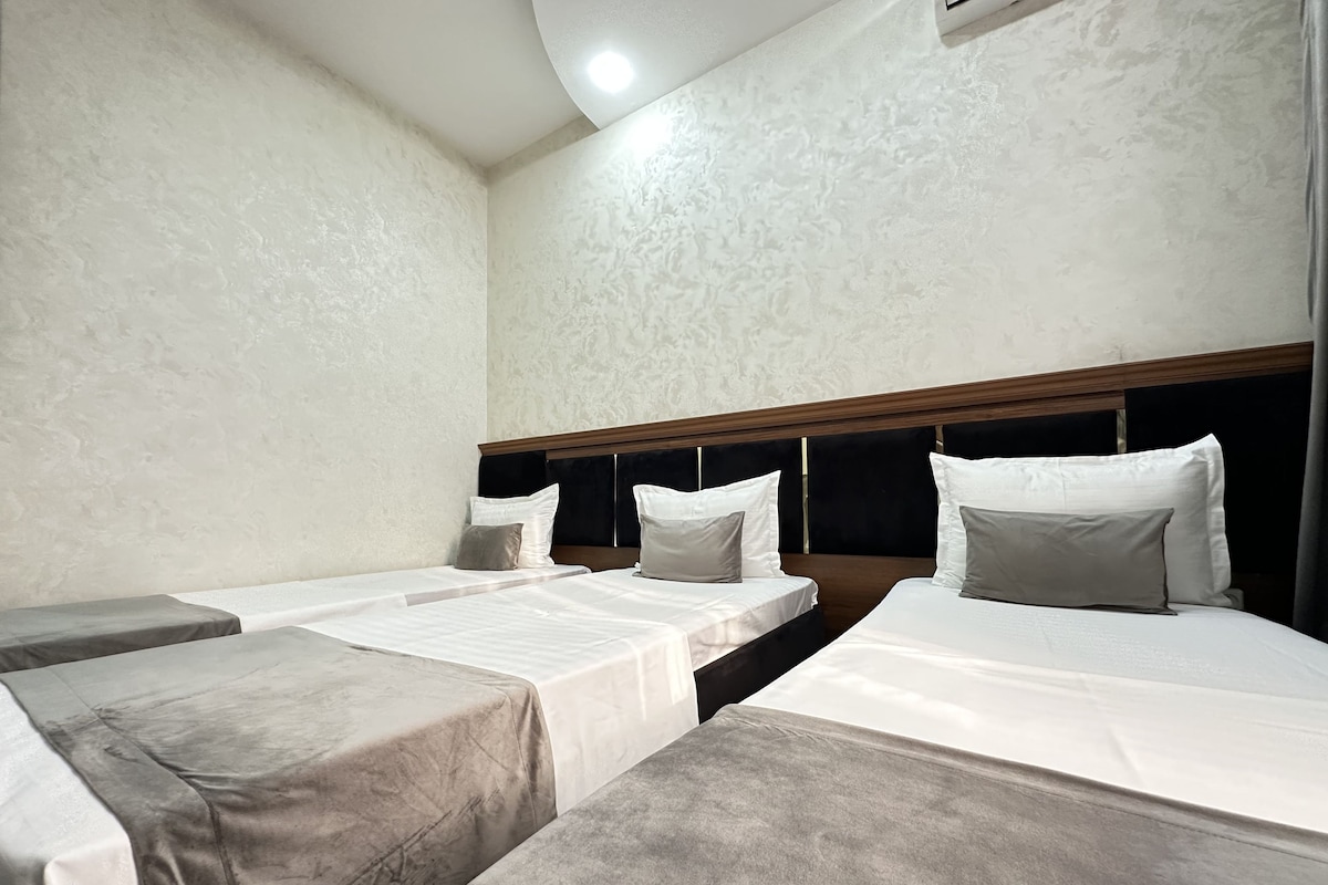 A hotel room with three beds, each with a headboard and pillows.
