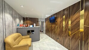 A modern hotel reception area with a reception desk, a plush armchair, and a wall-mounted TV. - Grand Zamin Hotel (Tashkent)