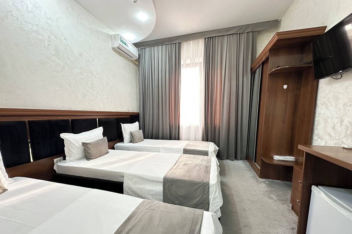 A hotel room with two beds, a TV, a wardrobe, and an air conditioning unit.