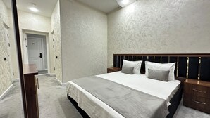 A bedroom with a large bed, a wooden headboard, and a nightstand with drawers. - Grand Zamin Hotel (Tashkent)