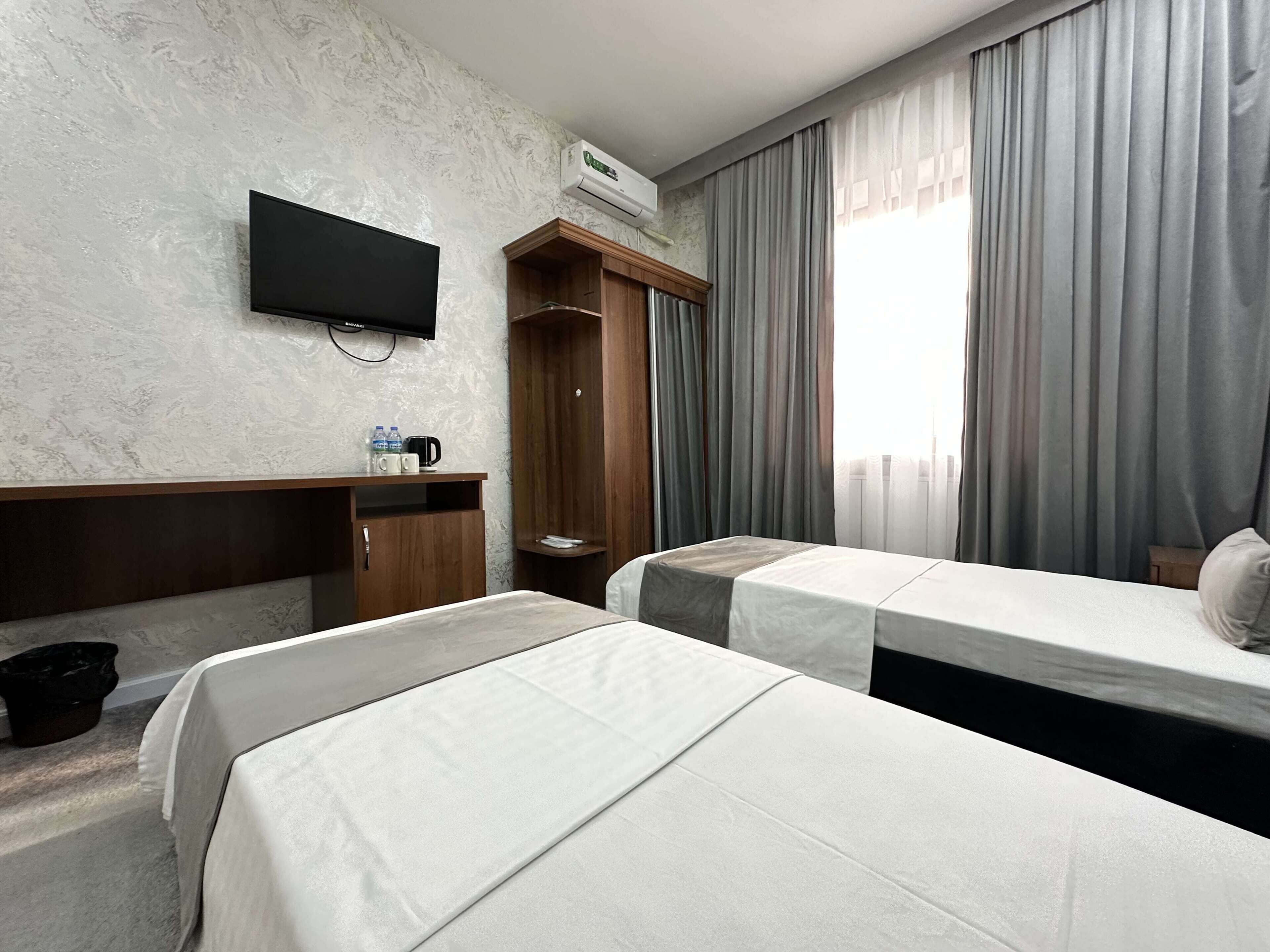 A hotel room with two beds, a TV, a wardrobe, and a window with curtains.