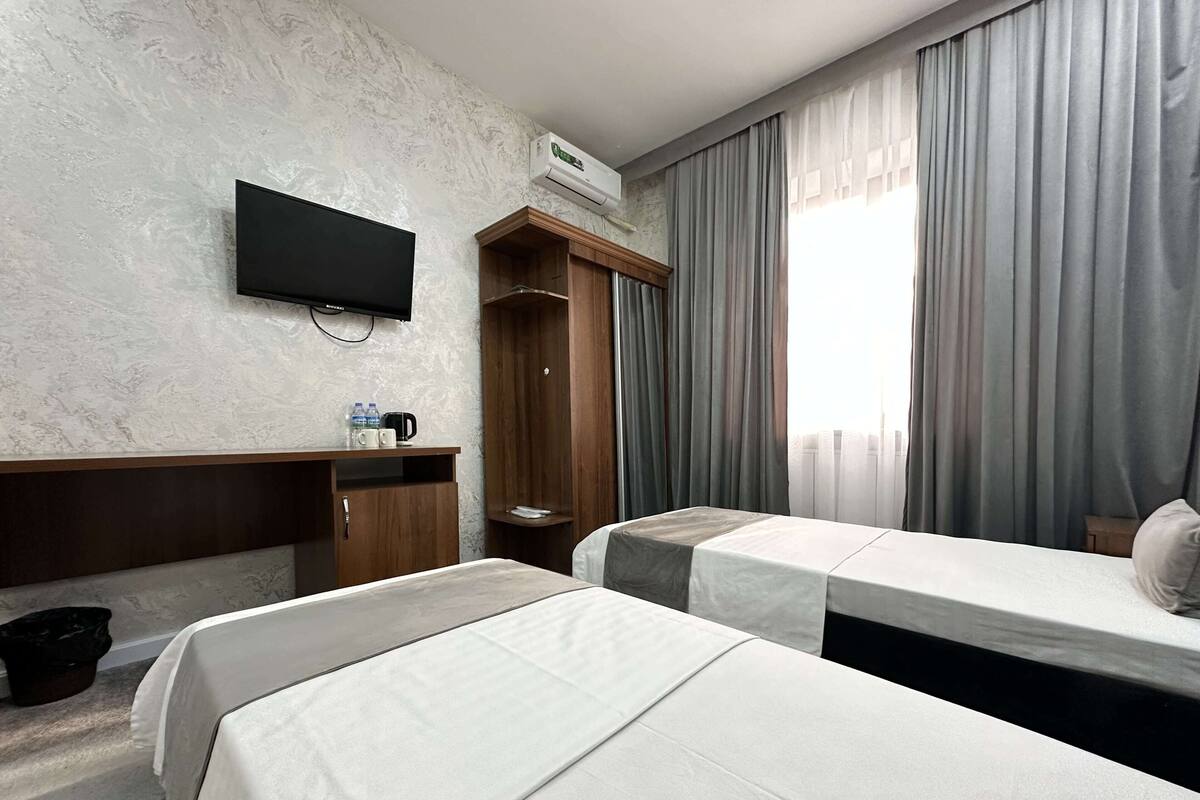 A hotel room with two beds, a TV, a wardrobe, and a window with curtains.