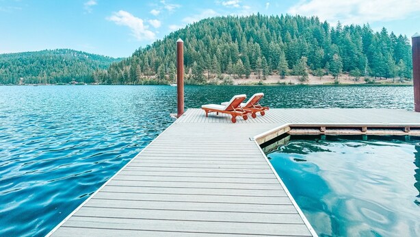 A wooden dock extending into a lake with two lounge chairs facing the water.