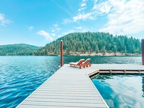 A wooden dock extending into a lake with two lounge chairs facing the water.