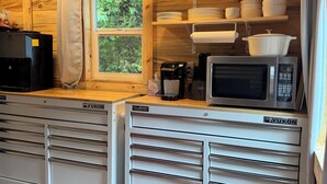 A compact kitchen with wooden walls, a window, and a white countertop with a microwave and a coffee maker.