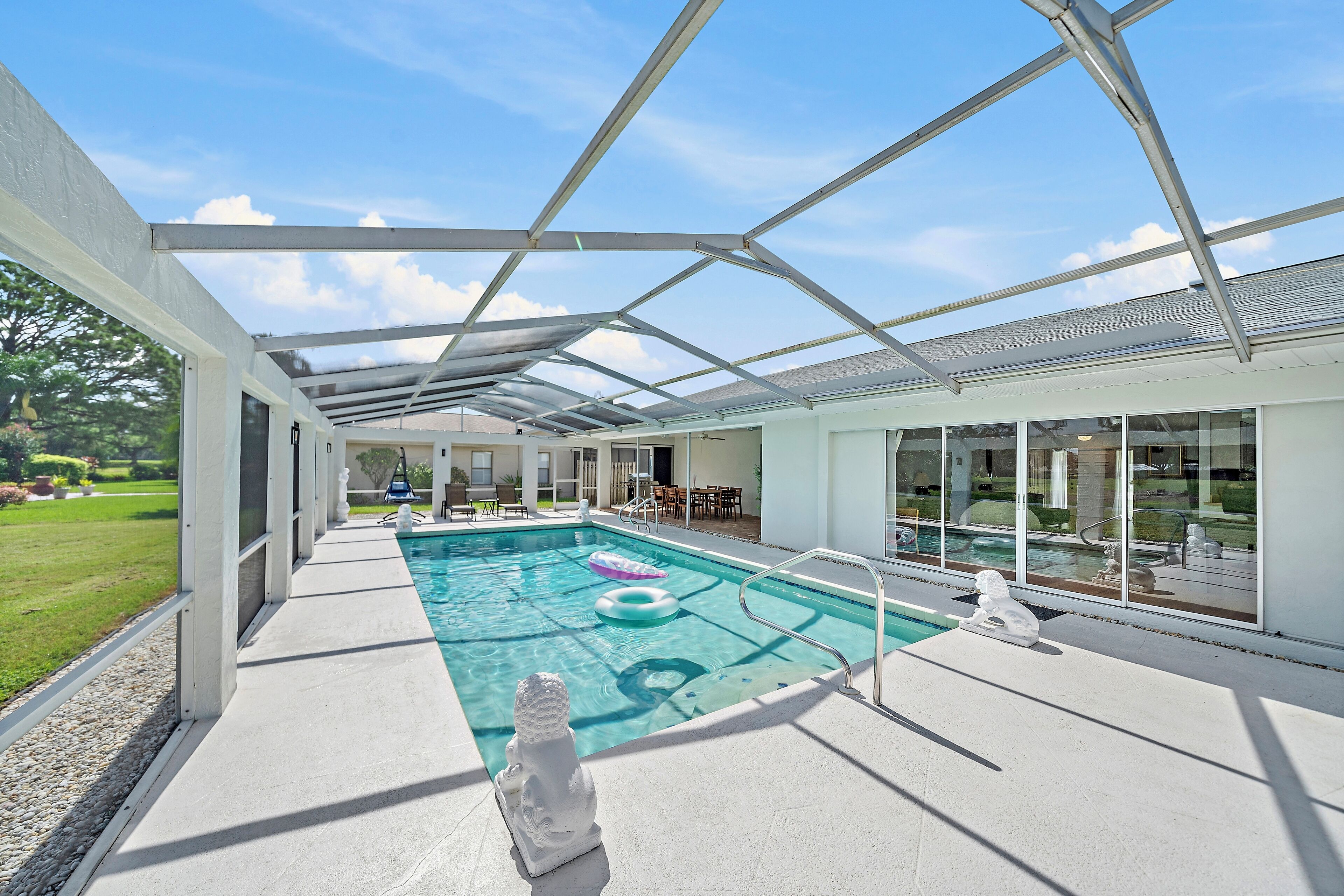An indoor swimming pool with a glass ceiling, surrounded by a poolside area with chairs and a statue.