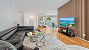 A modern living room with a sectional sofa, a glass coffee table, and a large flat-screen TV mounted on a wooden wall.