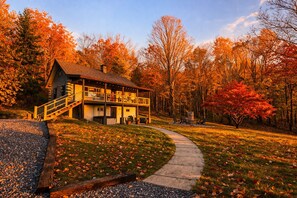 A two-story cabin with a balcony, surrounded by a forest with autumn foliage. - Cabin w/ Mini Horses, Fire Pit, Hot Tub, MTN Views (Sevierville)