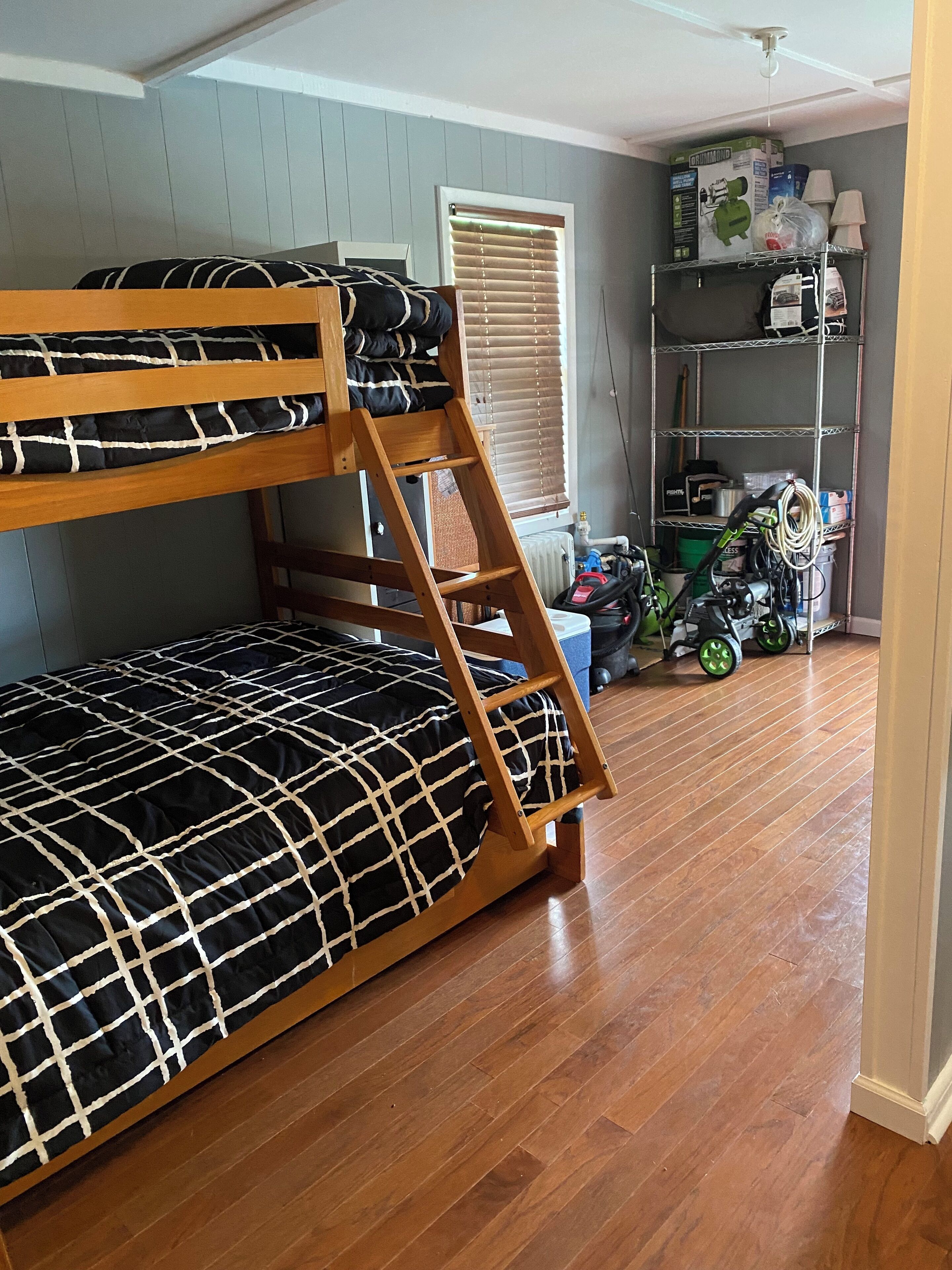 Een stapelbed met een zwart-wit geruit dekbed, een houten ladder en een raam met zonwering.