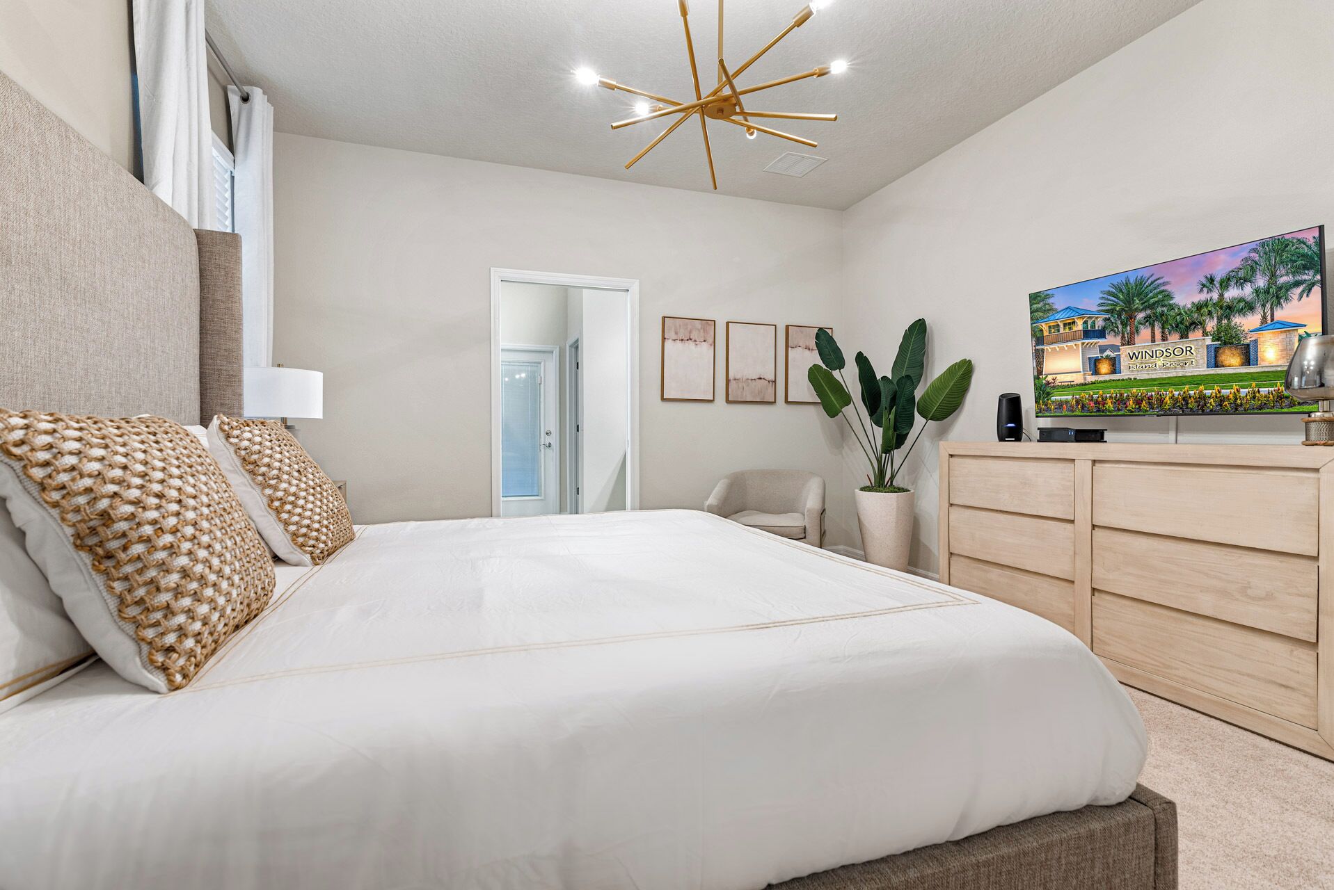 A bedroom with a large bed, a wooden dresser, a television, and a plant.