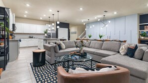 A modern living room with a grey sectional sofa, a glass coffee table, and a brown leather ottoman.
