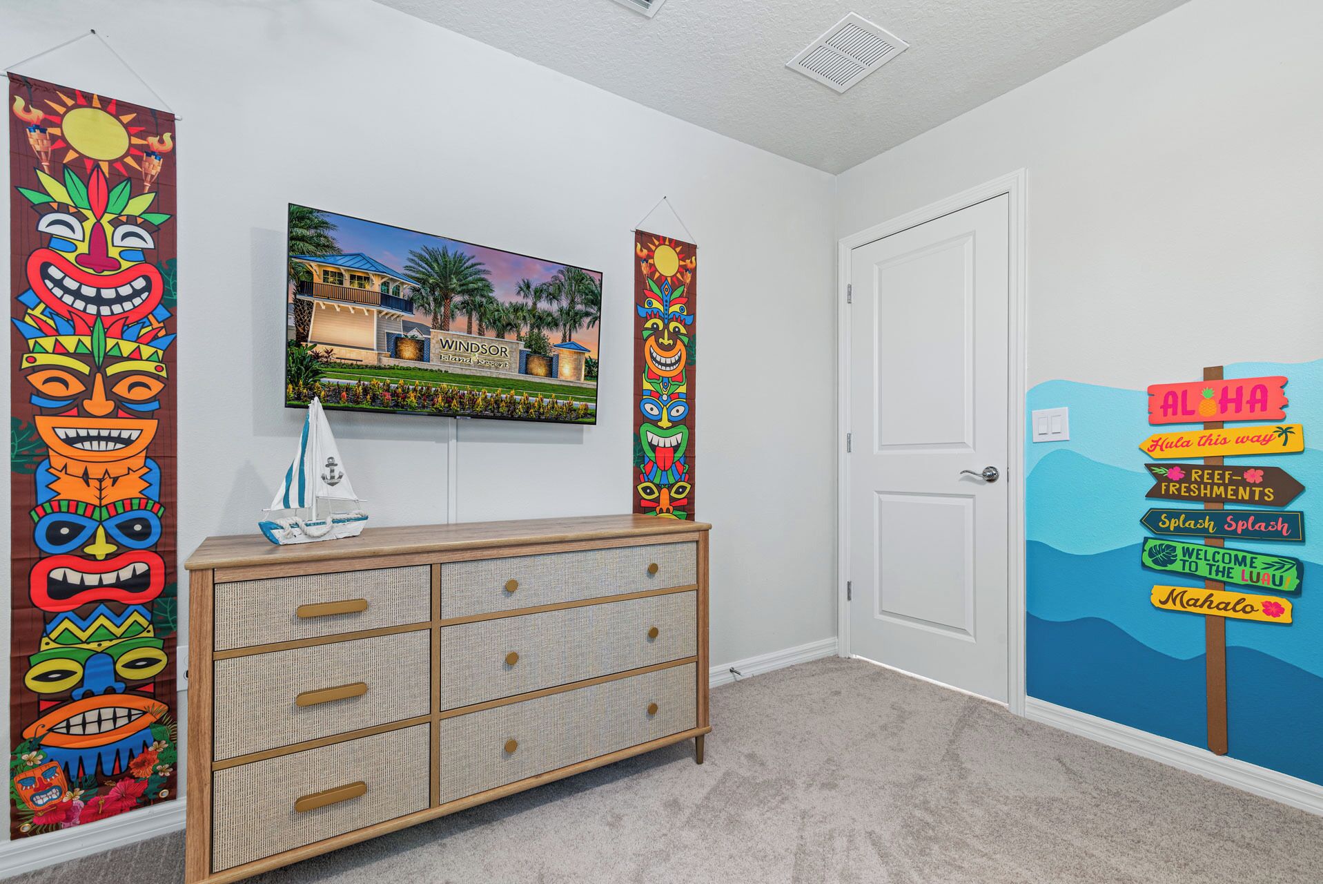 A room with a wooden dresser, a painting of a resort, and a wall mural with a signpost.