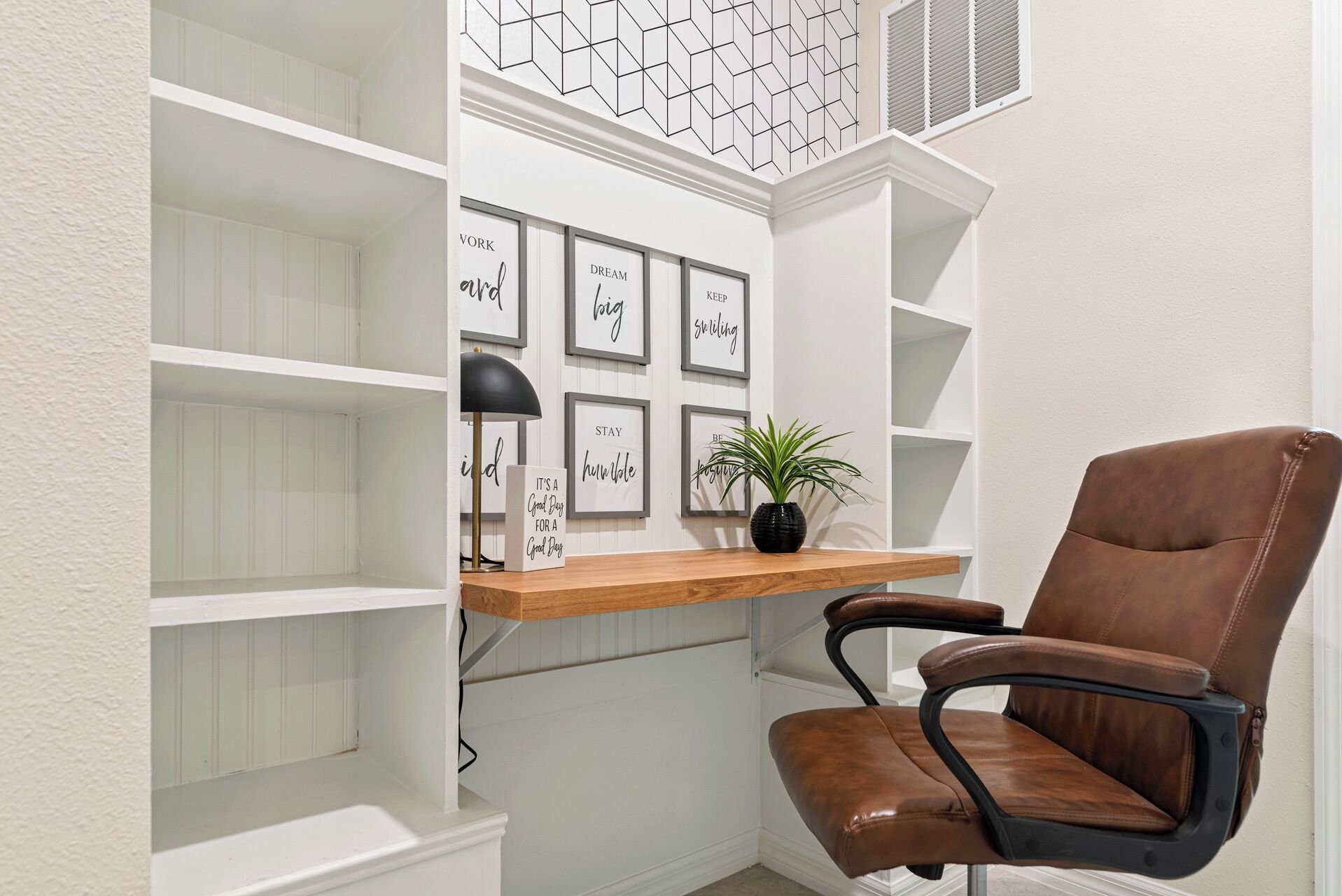 A corner office with a desk, chair, shelving, and framed inspirational quotes.