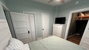 Une chambre à coucher avec un lit, une commode, un téléviseur et un placard.
