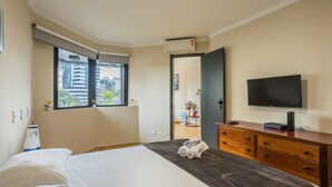 Habitación de hotel con cama, cómoda, televisor y ventana con vistas a edificios.