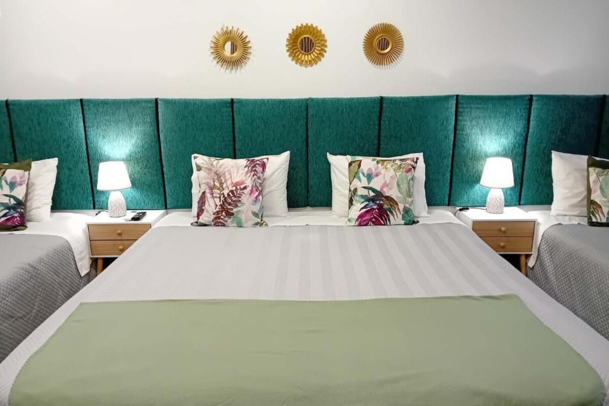 Una habitación de hotel con una cama grande, dos mesitas de noche y un cabecero verde.