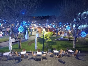 Un espacio al aire libre con mesas y sillas, rodeado de árboles decorados con luces.