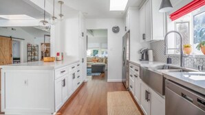 A modern kitchen with white cabinetry, a central island, and a view into the living area. - Adorable 3 bdr Home Universal Pool hot tub (Los Angeles)