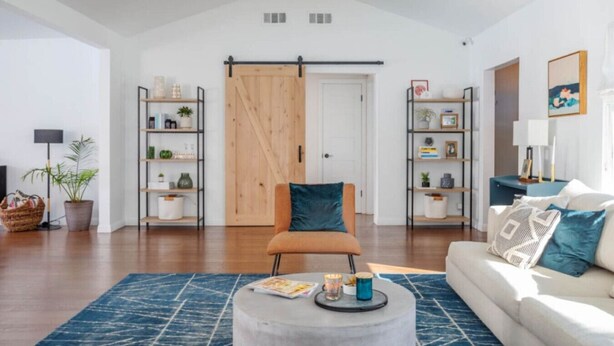 A modern living room with a sofa, a coffee table, and a chair. There are two shelves with plants and books, and a wooden door in the background. - Adorable 3 bdr Home Universal Pool hot tub (Los Angeles)
