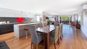 A modern kitchen with a red appliance, a dining area with a wooden table and leopard print chairs, and a large window offering a view of greenery.