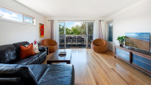 A modern living room with a black leather sofa, two wicker chairs, a wooden coffee table, and a TV on a wooden stand.