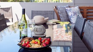 A dining table with a bottle of wine, glasses, a bowl of fruit, and a plate of food.